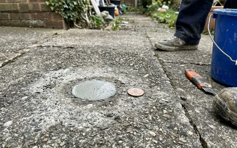 Close-up of a patched penny-sized injection port in weathered concrete with a coin for scale