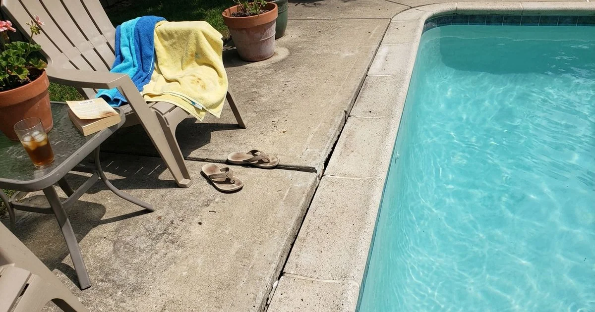 Concrete pool surround with a settled section beside the coping, pool water visible