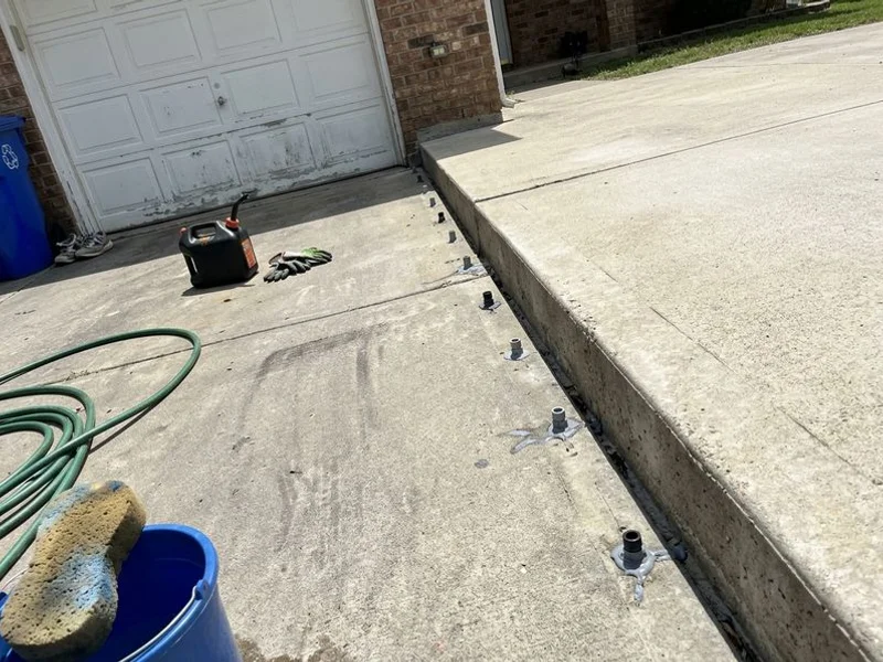A dropped driveway section beside a garage apron with a clear step at the joint and injection ports drilled in a row
