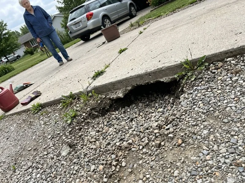 Eroded channel under a driveway edge where runoff has carried the base away