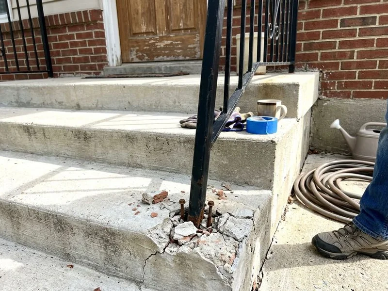 Loose handrail post at a settled concrete stoop with cracked mortar at the base