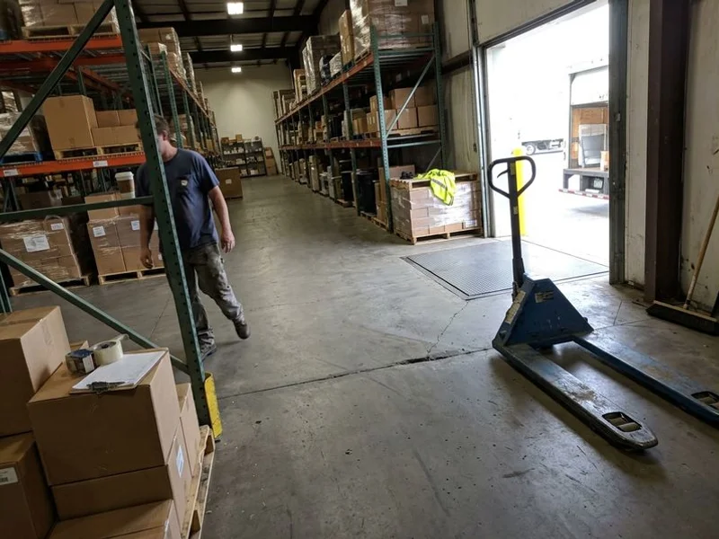 Warehouse floor with a visible dip near a loading dock door and a pallet jack beside it